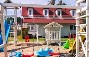 Ein Spielplatz mit Schaukeln, Rutschen und einem kleinen Spielhäuschen.