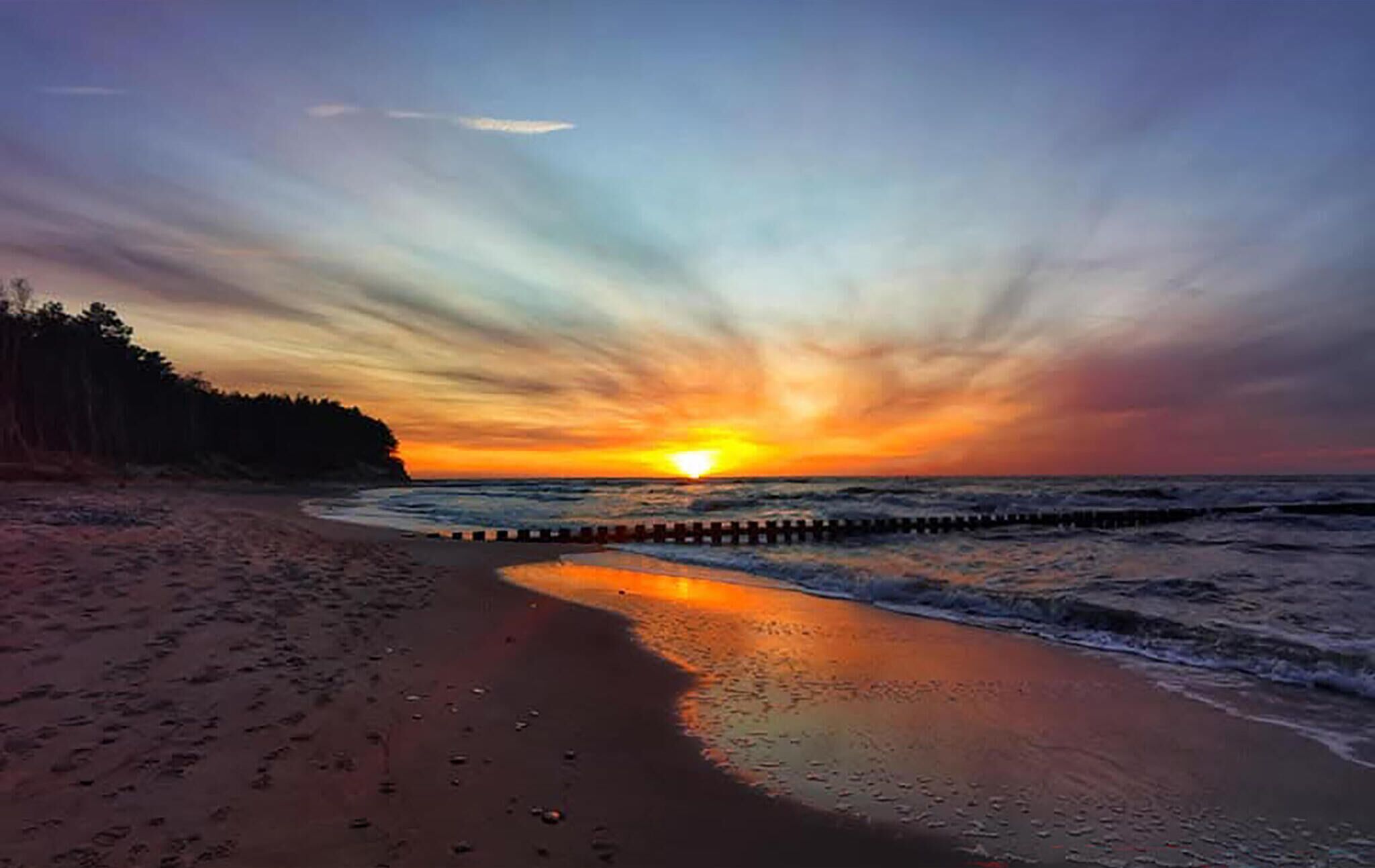 Una platja amb un capvespre, onades i un moll de fusta.