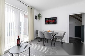 Una sala de estar moderna con comedor, un televisor montado en la pared y una botella de vino sobre una mesa.