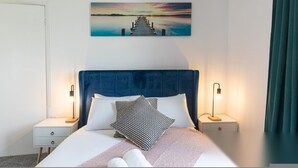 Una habitación de hotel con una cama, dos mesitas de noche, un cabecero y un cuadro de un muelle.
