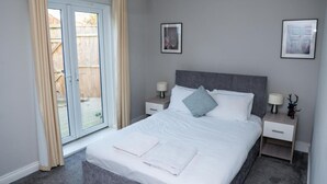 Un dormitorio con cama, dos mesitas de noche, una ventana con cortinas y dos cuadros en la pared.