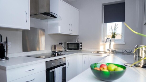 Una cocina moderna con armarios blancos, microondas, tostadora y lavamanos.