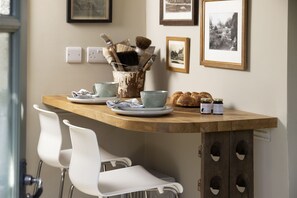 Uma bancada de cozinha com design rústico, apresentando uma mesa de madeira, cadeiras brancas e diversos utensílios de cozinha como pratos, copos e potes.