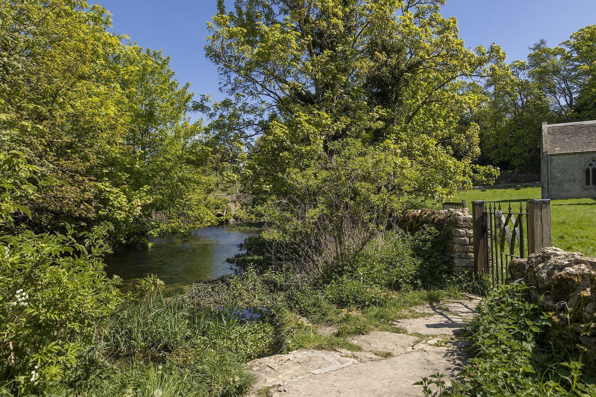 A stone bridge over a river, surrounded by lush greenery and a stone wall.