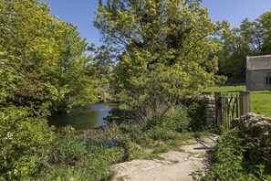 Un puente de piedra sobre un río, rodeado de exuberante vegetación y un muro de piedra.