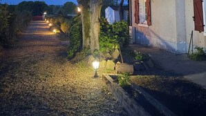 A rural pathway leading to a white building with red shutters, surrounded by trees and lit by ground lights. - Villa Les Tilleuls - Gîte 6 people Graçay Berry | Telecommuting & Family" - Telecommuting & Family (GRACAY)