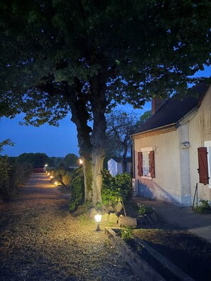 A rural pathway leading to a white building with red shutters, surrounded by trees and lit by ground lights. - Villa Les Tilleuls - Gîte 6 people Graçay Berry | Telecommuting & Family" - Telecommuting & Family (GRACAY)