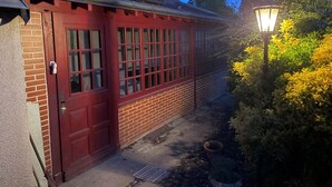 A red brick building with a red door and windows, a metal gutter, and a garden with yellow foliage and a street lamp. - Villa Les Tilleuls - Gîte 6 people Graçay Berry | Telecommuting & Family" - Telecommuting & Family (GRACAY)