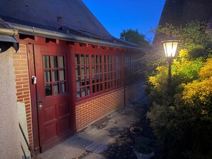 A red brick building with a red door and windows, a metal gutter, and a garden with yellow foliage and a street lamp. - Villa Les Tilleuls - Gîte 6 people Graçay Berry | Telecommuting & Family" - Telecommuting & Family (GRACAY)