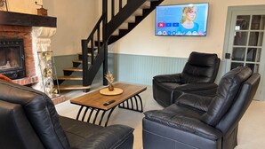 A living room with a fireplace, a black leather sofa, a coffee table, and a TV mounted on the wall. - Villa Les Tilleuls - Gîte 6 people Graçay Berry | Telecommuting & Family" - Telecommuting & Family (GRACAY)