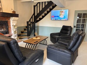 A living room with a fireplace, a black leather sofa, a coffee table, and a TV mounted on the wall. - Villa Les Tilleuls - Gîte 6 people Graçay Berry | Telecommuting & Family" - Telecommuting & Family (GRACAY)
