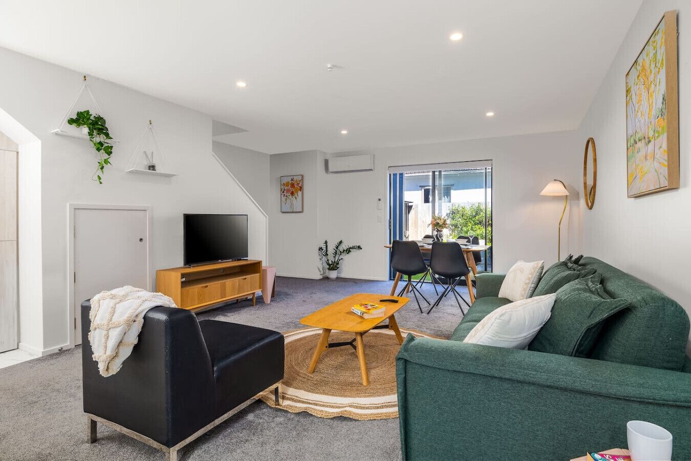A modern living room with a sofa, coffee table, TV, and a dining area with chairs.