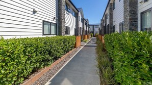 Una strada residenziale con case moderne, un vialetto in cemento e siepi curate.