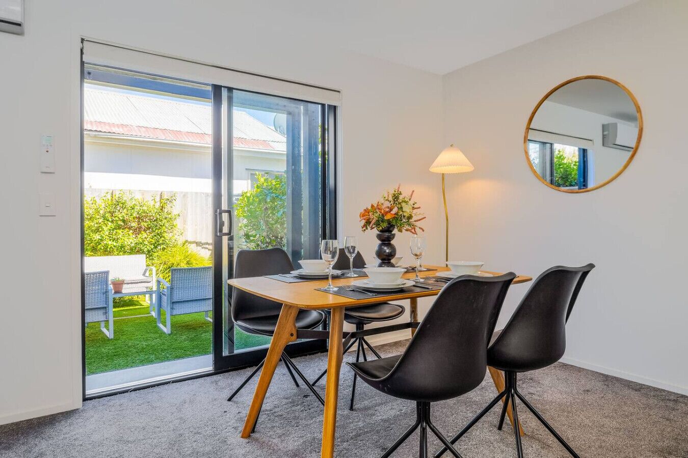 Et værelse med et spisebord, en lampe, et spejl og en skydedør til en have.