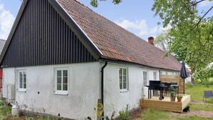 Valkoinen talo, jossa on musta katto, puinen terassi ja puutarha.