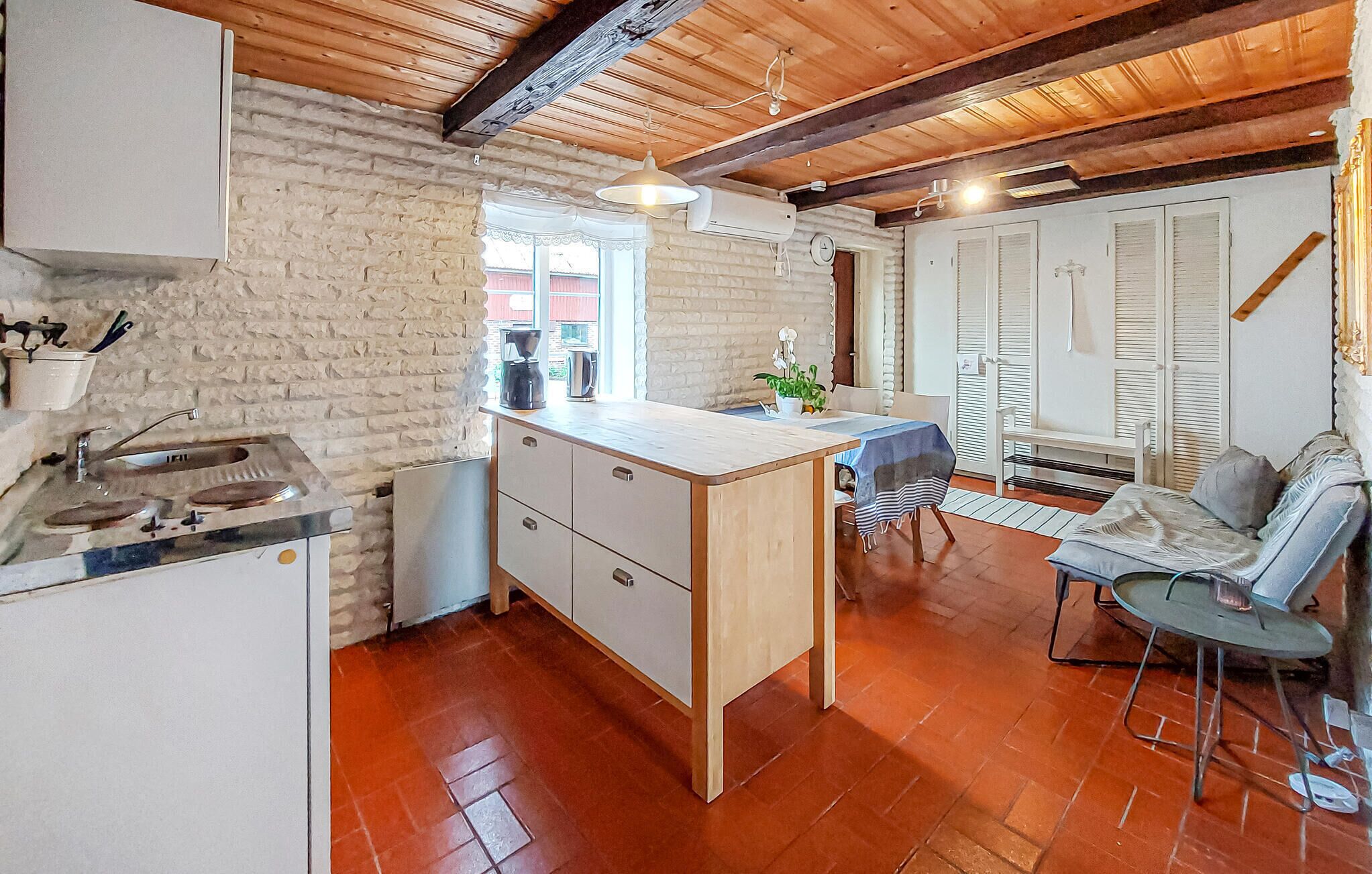 Eine kompakte Küche mit Holzbalkendecke, ein kleiner Essbereich mit Tisch und Stühlen sowie eine Sitzecke mit Sofa.