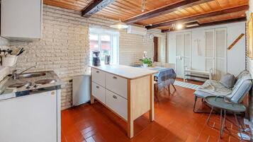 Eine kompakte Küche mit Holzbalkendecke, ein kleiner Essbereich mit Tisch und Stühlen sowie eine Sitzecke mit Sofa.