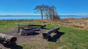 Un espace de pique-nique aménagé au bord du lac, avec un foyer, des bancs et une vue sur l’eau.