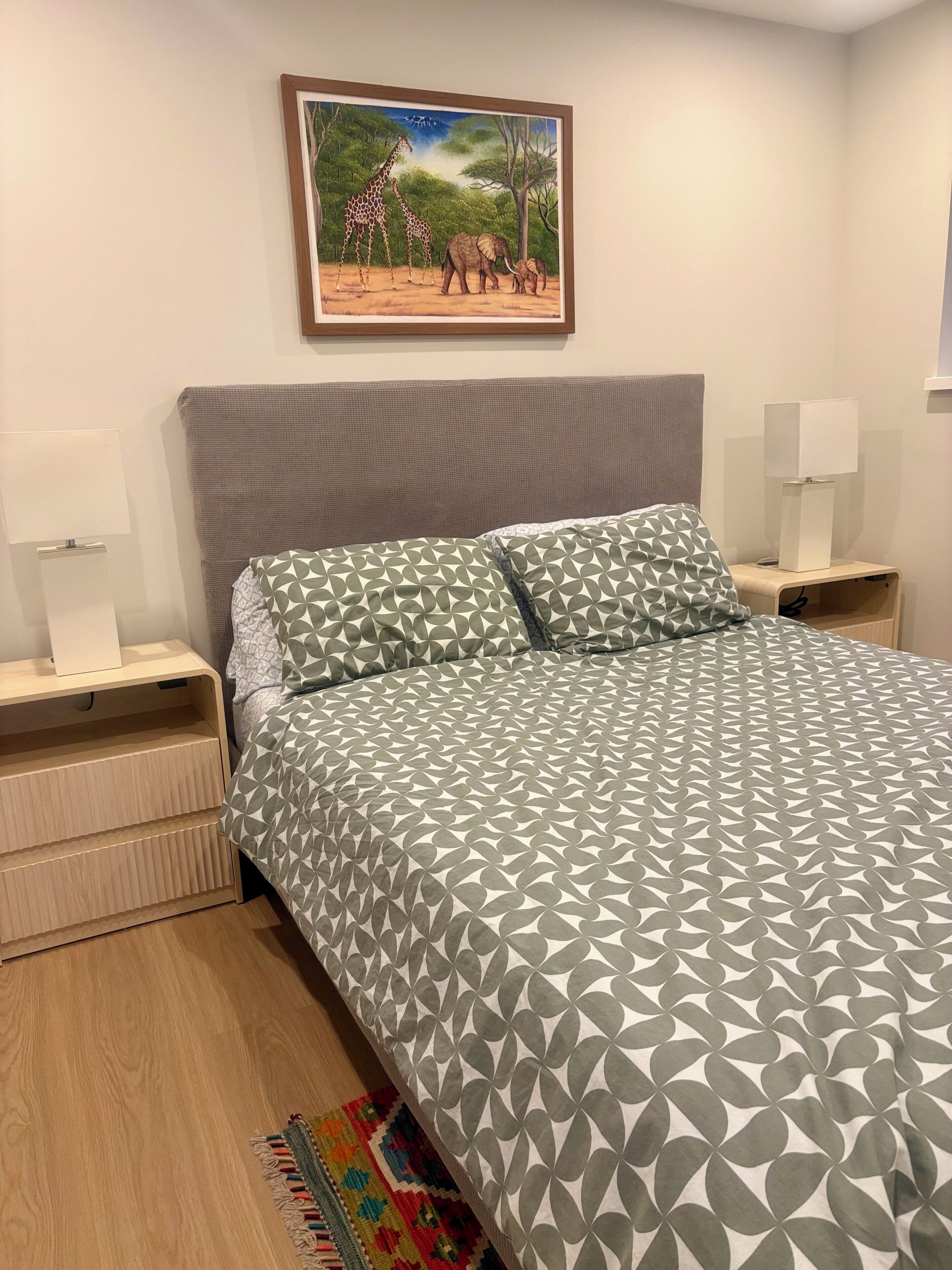 Una camera da letto con un letto, due comodini, una lampada, un quadro incorniciato appeso al muro e un tappeto decorato.