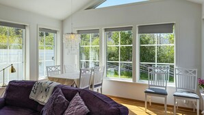 Ein heller Raum mit großen Fenstern, einem violetten Sofa, weißen Stühlen und einem Esstisch.