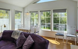 A bright room with large windows, a purple sofa, white chairs, and a dining table. - Stunning home in Gotlands Tofta (Gotlands Tofta)