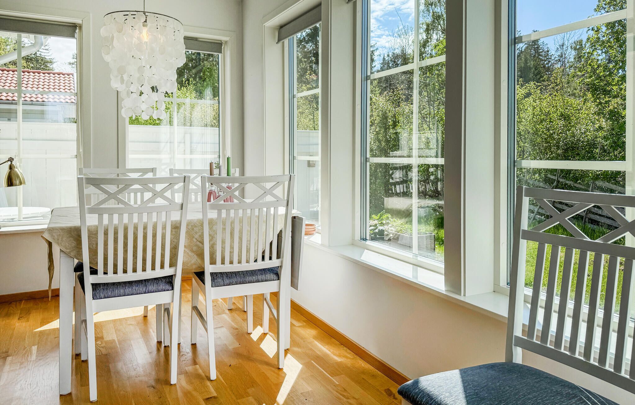 Un comedor con sillas blancas, una mesa y ventanas amplias con vistas a zonas verdes.