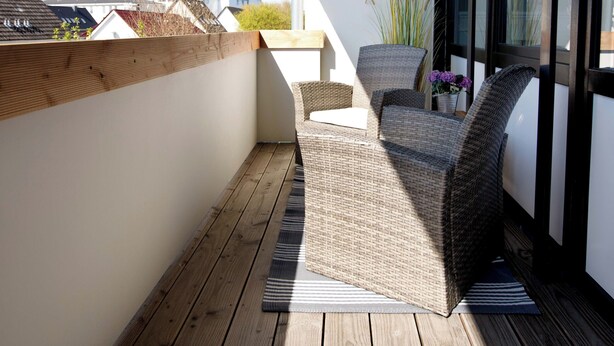En balkon med fletmøbler, en potteplante og et vægmonteret lysarmatur.