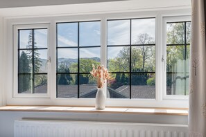 Ein Zimmer mit einem großen Fenster, einem Heizkörper darunter und einer Vase mit Trockenblumen auf der Fensterbank.