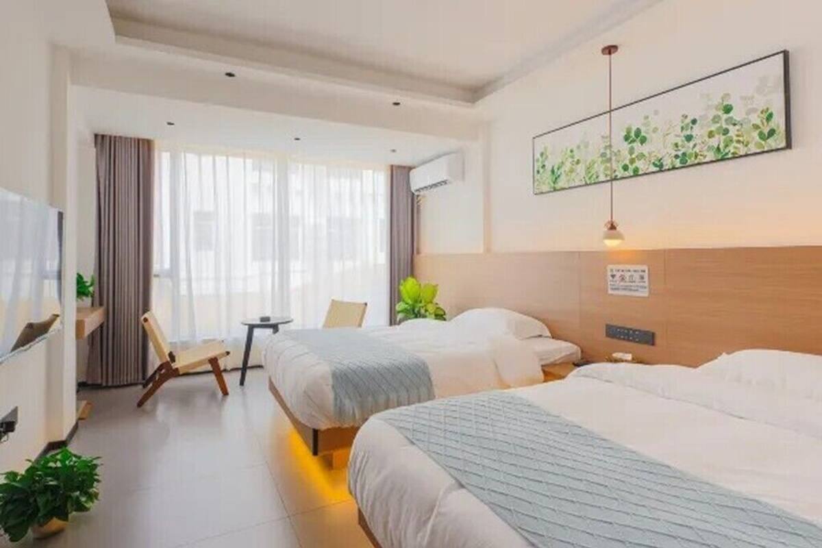 Ett hotellrum med två sängar, ett skrivbord, en stol och ett stort fönster med gardiner.
