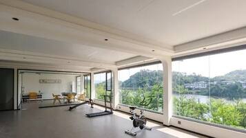Amplia habitación con ventanas grandes, equipo de ejercicio y vistas a un lago y colinas.