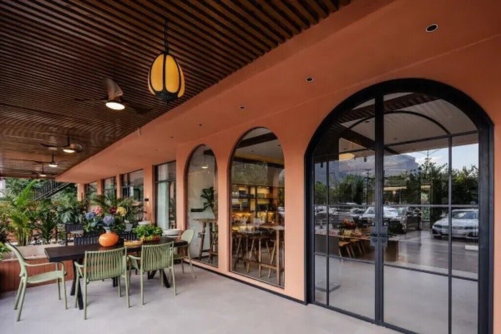 A covered outdoor seating area with tables and chairs, large windows, and a view of the parking lot.