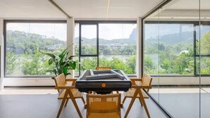 Una habitació amb una taula gran i cadires, una planta en test i vista a un paisatge verd a través de grans finestres.