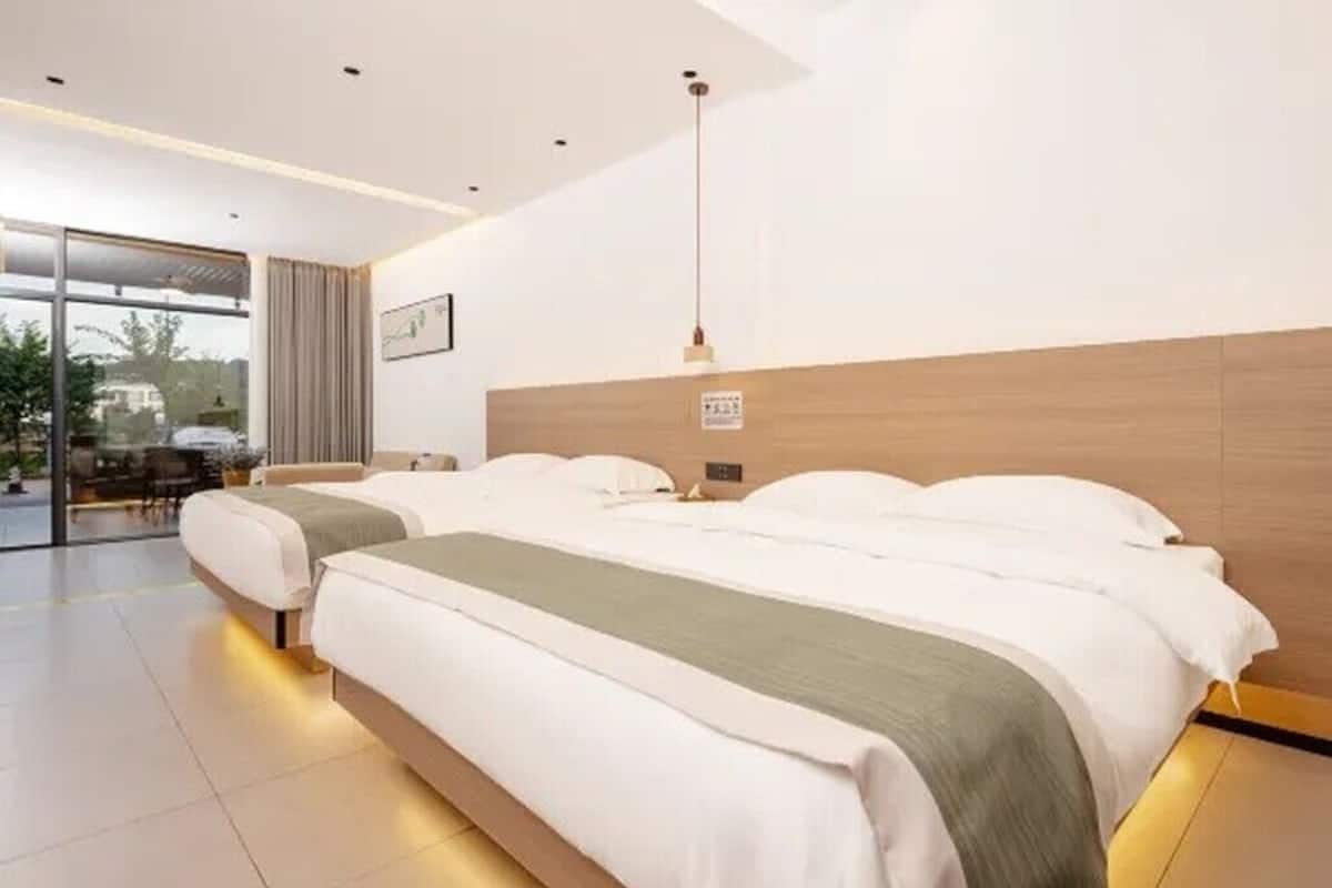 Ett modernt hotellrum med två sängar, ett stort fönster och en skjutdörr som leder ut till ett utomhusområde.