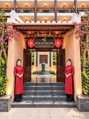 A hotel entrance with a sign reading 'Hoi An Moon,' a traditional architectural style with a tiled floor, and two waitresses in red uniforms. - HOI AN MOON PREMIUM BOUTIQUE HOTEL & SPA (Da Nang)