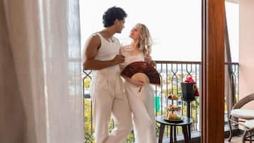 Um casal em uma varanda com vista, uma mesa pequena com comida e um ventilador.