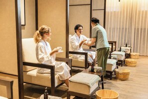 A spa room with individual seating, wooden tubs, and a person attending to guests. - HOI AN MOON PREMIUM BOUTIQUE HOTEL & SPA (Da Nang)