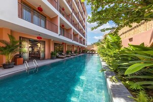 A hotel with a swimming pool, outdoor seating, and lush greenery.