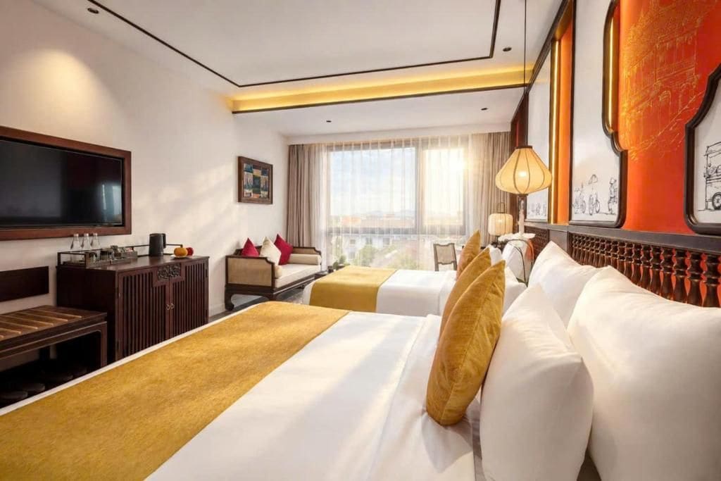A hotel room with two beds, a television, a desk with a lamp, and a window with curtains.