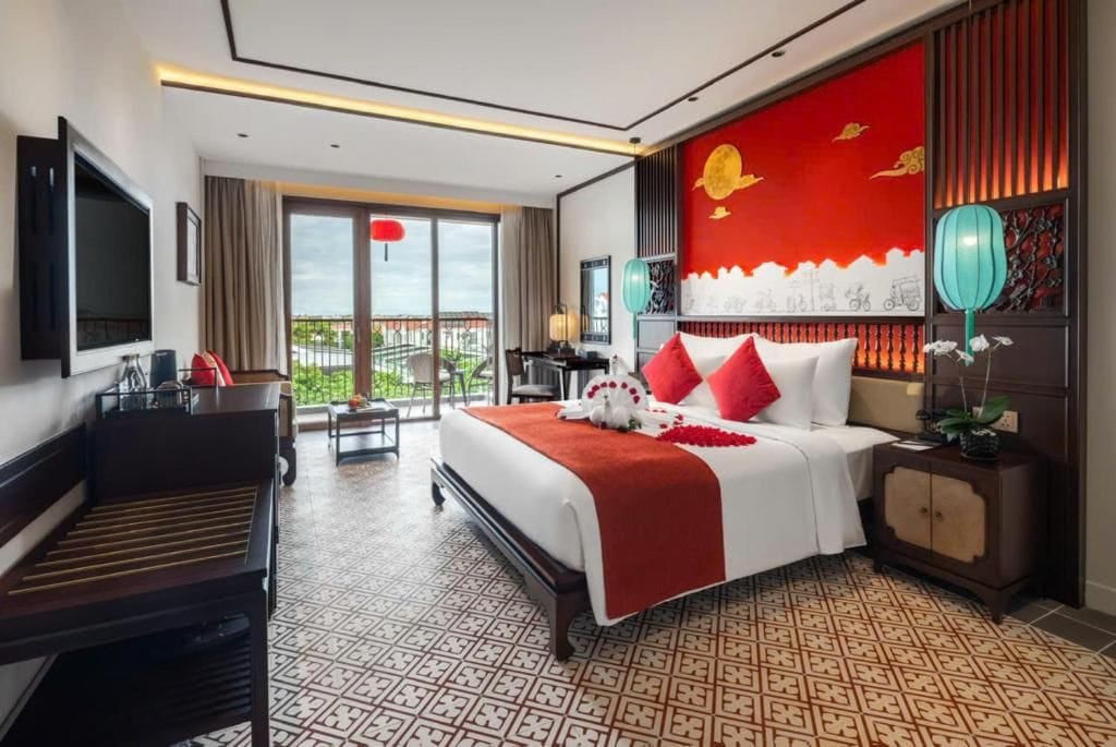 Ein Hotelzimmer mit Bett, Schreibtisch, Fernseher, Balkon und Blick auf die Stadt.