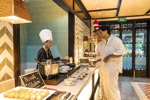 A buffet setup with a noodle station, a chef preparing food, and a sign indicating the noodle station.
