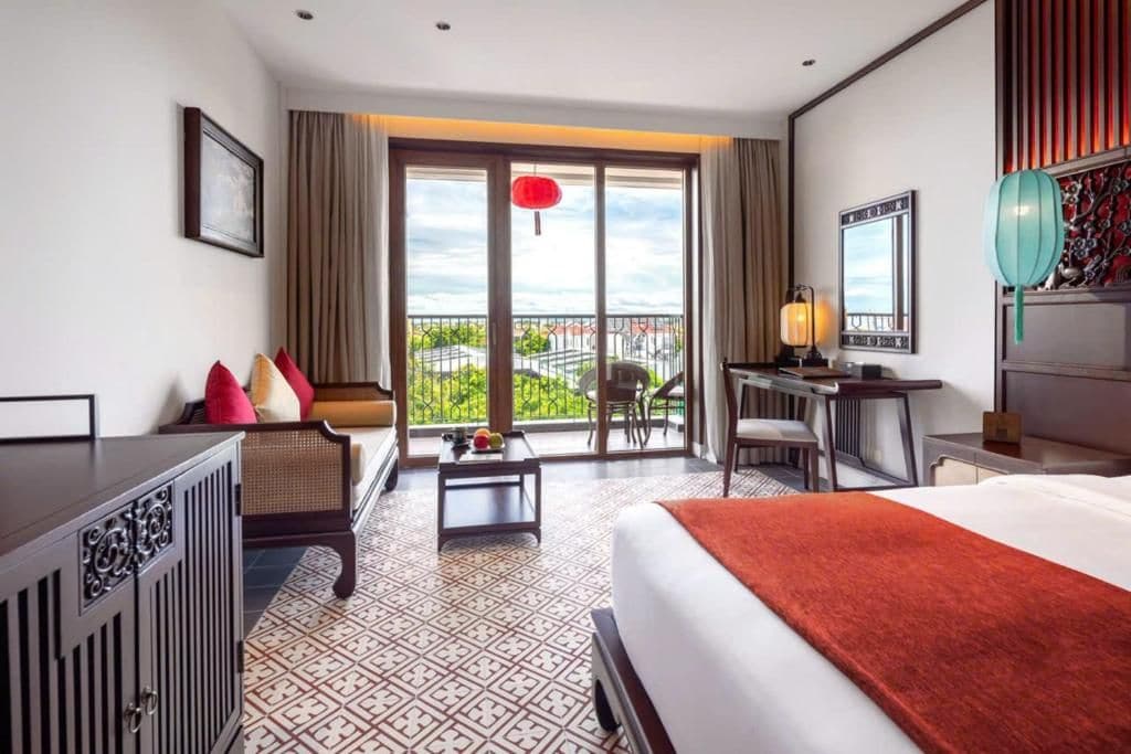 Quarto de hotel com cama, escrivaninha, cadeira e vista para o exterior.