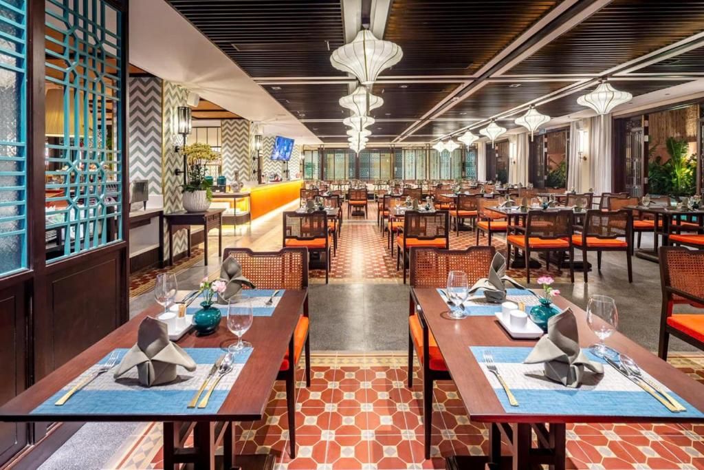 Restaurante com várias mesas de jantar, cada uma posta com talheres e copos, e piso estampado.