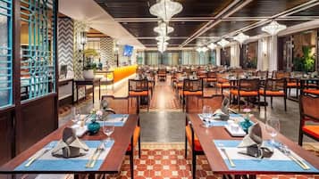 Restaurante com várias mesas de jantar, cada uma posta com talheres e copos, e piso estampado.