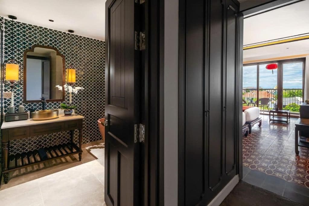 A modern bathroom with a dark wooden door, a mirror, and a vanity with a sink and towel rack.