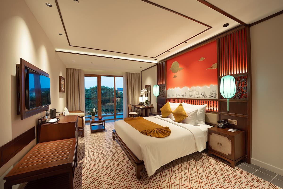 A hotel room with a bed, bedside table, desk, and a large window.