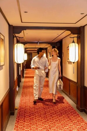 A hotel corridor with a patterned carpet, wall-mounted lamps, and framed artwork. - HOI AN MOON PREMIUM BOUTIQUE HOTEL & SPA (Da Nang)