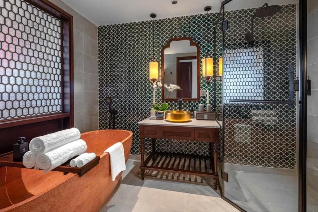 Une salle de bain avec une baignoire en bois, un lavabo avec un miroir et un mur décoré d’un motif.