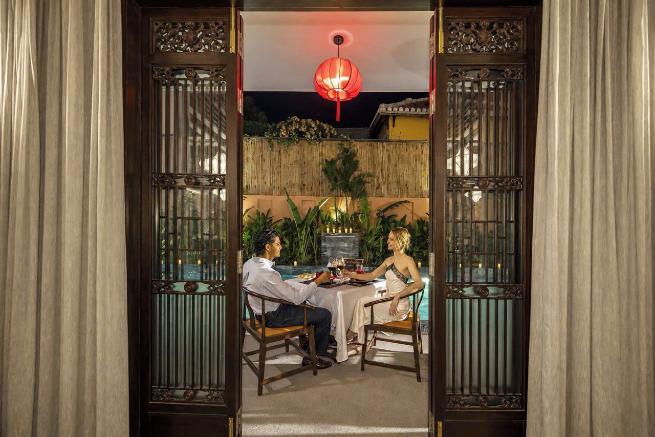 Una pareja cenando en una mesa con vista a un jardín y un farol decorativo encima.
