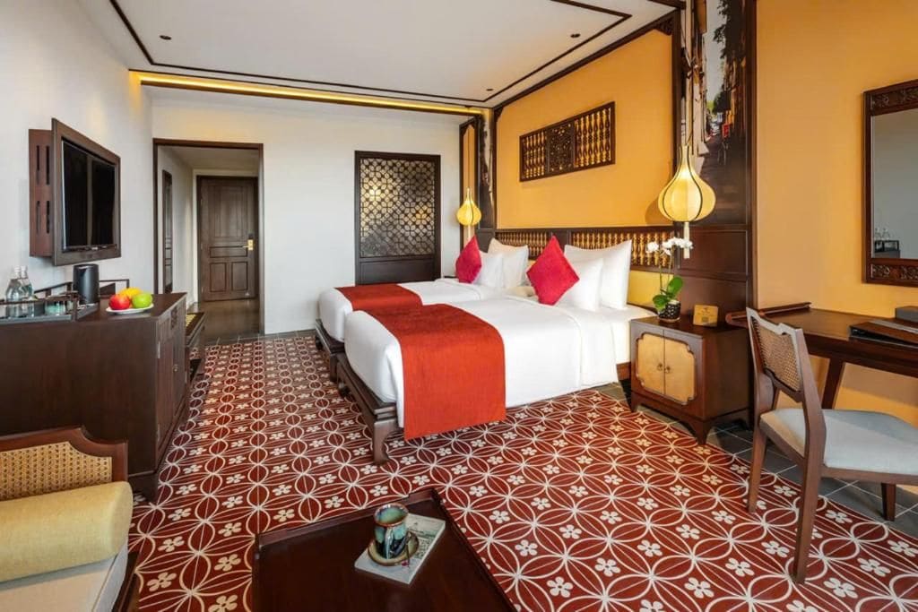 A hotel room with a bed, a desk, a chair, a television, and a patterned floor.
