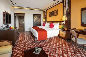 A hotel room with a bed, a desk, a chair, a television, and a patterned floor.
